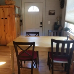 A wooden dining table with three chairs is in a room with hardwood floors, a cabinet, and a front door with a window.