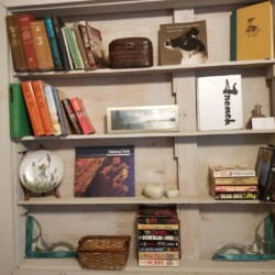 Wooden bookshelf filled with books, a cowboy hat, small decorative items, and a pair of candle holders.