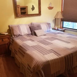 A neatly made bed with patterned bedding, flanked by wooden nightstands and a lamp, in a warmly lit bedroom.