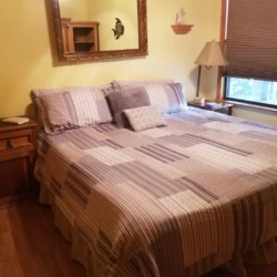 A neatly made bed with patterned bedding, flanked by wooden nightstands and a lamp, in a warmly lit bedroom.