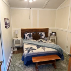 A bedroom with a quilted bed, wooden headboard, side tables with lamps, and a small bench at the foot of the bed.