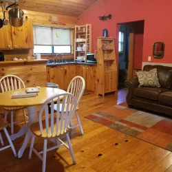 Cozy cabin interior with wooden furniture, dining table, kitchen area, and brown sofa on a rug over wooden floor.