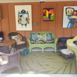 Outdoor seating area with wicker furniture and colorful animal wall art on a brick wall.