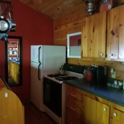 Rustic kitchen with wooden cabinets, a white refrigerator, pots hanging, and a small counter. Walls are red with a mirror.