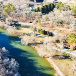 Aerial view of a river winding through a rural landscape with scattered trees and small structures visible along the banks.