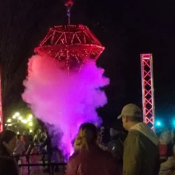People gather at night around a red and purple lit structure emitting smoke at an outdoor event.