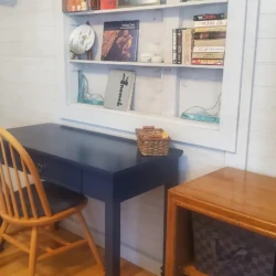 Wooden chair at blue desk with books and decorations on wall-mounted shelves, next to a TV on a wooden stand.
