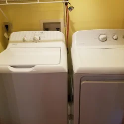 A white washer and dryer set in a laundry room with yellow walls and a shelf above.