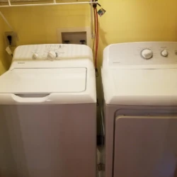 A white washer and dryer set in a laundry room with yellow walls and a shelf above.