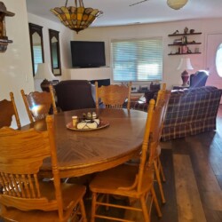 A dining room with a wooden table and chairs, a plaid sofa, a flat-screen TV, and a stained glass ceiling light.