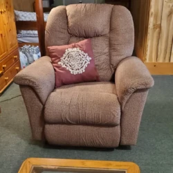 A brown recliner chair with a decorative pillow is placed in a cozy living room with wooden walls and a glass coffee table.