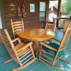 A wooden table with four rocking chairs on a porch with green flooring and a wall with decorative items.