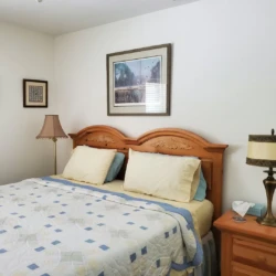 Cozy bedroom with a wooden headboard bed, floral lamps, and framed art on white walls.