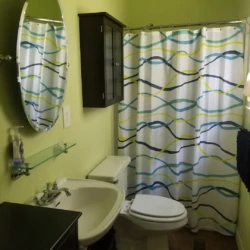 Compact bathroom with a sink, toilet, and a shower curtain featuring wavy patterns in blue, green, and yellow.