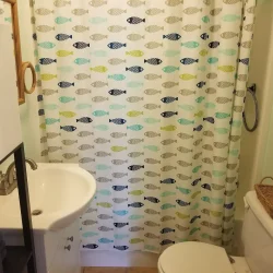 Small bathroom with a fish-patterned shower curtain, white sink, toilet, wicker basket, and pale green wall with a towel.