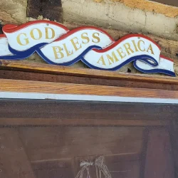 A wooden sign above a screen door says "God Bless America" with a wavy red, white, and blue design.