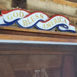 A wooden sign above a screen door says "God Bless America" with a wavy red, white, and blue design.
