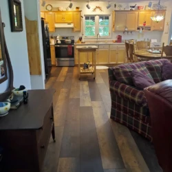 A cozy kitchen and living space with wooden cabinets, a dining table, plaid sofa, and various decorations on display.