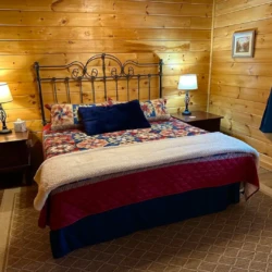 A cozy bedroom with a metal-framed bed, colorful quilt, two nightstands with lamps, wooden walls, and a window with curtains.