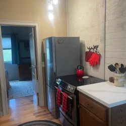 A modern kitchen with stainless steel appliances, red accents, and a view into a bedroom.