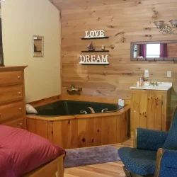 Bedroom with wooden walls, a bed, armchair, wooden hot tub, vanity, and decor saying "LOVE" and "DREAM" on the wall.