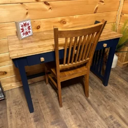 Wooden desk with a matching chair against a paneled wall, featuring a decorative tile, DVDs, and a plant in the corner.