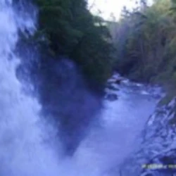 Waterfall cascading into a rocky river surrounded by lush greenery.