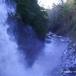 Waterfall cascading into a rocky river surrounded by lush greenery.