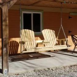 Wooden bench swing on a porch, supported by chains, beneath a wooden pergola, with a gravel foreground.