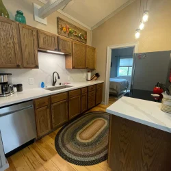A kitchen with wooden cabinets, white countertops, a dishwasher, a coffee maker, a rug, and pendant lights.