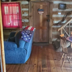 Cozy log cabin interior with wooden floors, a blue armchair, and rustic decor including a door with an American flag decoration.