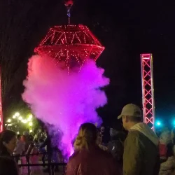 A red glowing structure emits purple smoke at night, surrounded by onlookers.