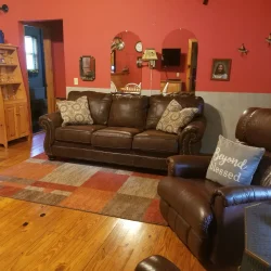 Living room with brown leather couch and recliner, red walls, wooden floor, and a "Beyond Blessed" pillow on the recliner.