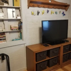 Living room with a TV on a wooden stand, shelves with books and games, and a decorative butterfly wall display.