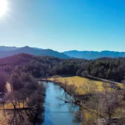 Aerial view of a river winding through a forested landscape with mountains in the background under a clear blue sky.