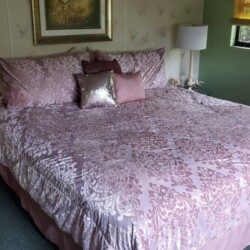 Bedroom with a king-size bed, floral-patterned pink bedding, two pillows, a sequin cushion, and a lamp by the bedside.