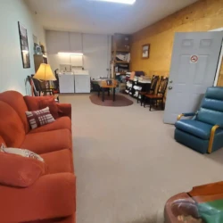 Room with red sofa, blue recliner, table, chairs, and a lamp. Laundry appliances are visible near the back wall.