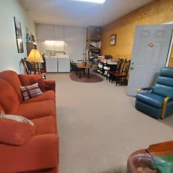 Room with red sofa, blue recliner, table, chairs, and a lamp. Laundry appliances are visible near the back wall.