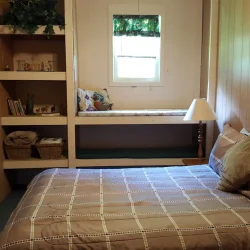 Small bedroom with wooden walls, a bed with checkered bedding, a built-in window nook, and wall art featuring horses.