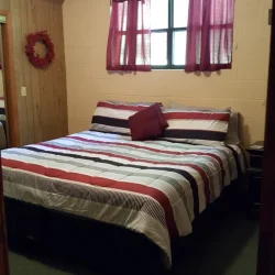 Cozy bedroom with a striped bedspread, maroon curtains, a wall-mounted wreath, and a ceiling fan.